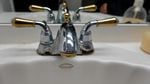 A silver and gold faucet above a sink shows signs of corrosion near its base.