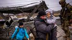 A man carries a child as he helps a fleeing family across a bridge destroyed by artillery, on the outskirts of Kyiv, Ukraine.