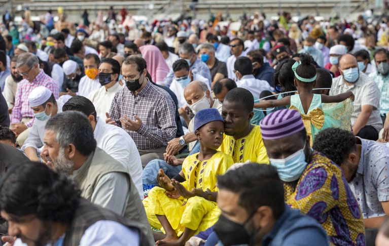 Muslim community members gather at Hillsboro stadium in Portland, Oregon for a prayer and festivities celebrating Eid Al-Adha. They raise their hands to pray at the end of the sermon before celebrations begin.