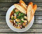 A bowl of clams in broth with chopped greens and bread.