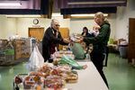 A woman holding a child hands another woman packaged food at a church set up as a food bank.