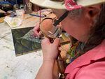 Portland artist Carolyn Garcia applies tiny highlights to a painting using a hand-held magnifying glass.
