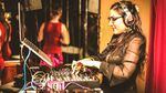A DJ works her gear while wearing headphones and a stylish dress.