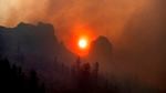 The sun appears orange and hazy, visible between mountain peaks and through a cloud of thick smoke.