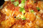A close-up of tater tots topped with cheese and sliced green onions