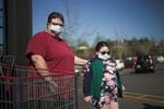 Two people wear face masks near a supermarket shopping cart.