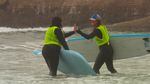 In this image captured from video footage, Siletz tribal member Kimberly Lane, left, high-fives professional surfer Kelly Potts as she wraps up her first surfing experience at Otter Rock on the Oregon coast.
