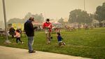 Families stand outside at the Jackson County Expo and read the news as the air is thick with wildfire smoke.