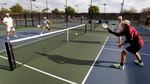 Four people on an outdoor court play a game of pickleball.