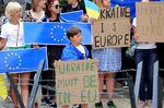 Adults and children stand holding European Union flags and signs supporting Ukraine's efforts to join the EU.