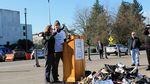 Gov. Brown stands with man at lectern and throws a shoe onto a pile of shoes