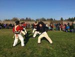 A 2018 reenactment at Fort Vancouver National Historic Site of a mid-19th century “Brigade” when the company employees returned to the fort after months of trapping furs in outlying areas. Both Navy sailors and the Marines trained in the use of cutlasses (a type of saber). In the photo, the Royal Marines are in red uniforms, Royal Navy in blue. At front right, Instructor-at-Arms Jeff Richardson of Academia Duellatoria. The reenactors are conducting a partner drill.