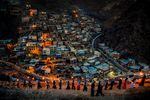 A line of men and women with torches walk along a ridge above a city nestled in the mountainside in Kurdistan. 