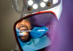 The gloved hands of a dental worker can be seen reflected in a mirror as they clean the teeth of a patient.