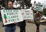 Opponents of a plan to sell the Elliott State Forest hold signs outside an Oregon State Land Board meeting.