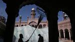 Two people work with cleaning tools while the minaret of a mosque rises in the background behind them.