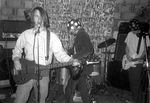 Slim Moon (left: vocals, bass) performing along with Billy Karren (right: guitar), Kurt Cobain (center: guitar), and Dave Grohl (obstructed: drums). Cobain and Grohl, of Nirvana, joined Moon and his band Witchypoo for a performance at The Mushroom in Olympia, Wash., on Feb. 9, 1991.