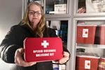 A person holds a red box open. The lid of the box reads "opioid overdose naloxone kit"