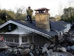 A firefighter stands on the roof of a house submerged in mud and rocks, Jan. 10, 2018, in Montecito, Calif.
