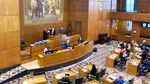 A view of the Oregon Capitol House floor seen from above shows legislators and staff at desks and at the front of the room with a very tall painting on the wall in the background.