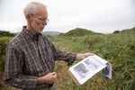 Historian Jerry Sutherland looks at old pictures of Bayocean as he walks the dunes in search of the town that used to stand under his feet. 