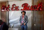 A man with a complete cowboy outfit poses underneath a bright red sign in a tent.