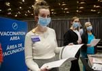 Jenna Mihelich, left, and Galina Leonchik, center, review check in materials before the opening of a COVID-19 vaccination clinic being held at the Oregon Convention Center, Jan. 27, 2021. The clinic will run at least through this week and aims to give 2,000 vaccinations per day to pre-registered recipients. 