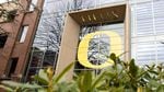 A glass-walled academic building has a large yellow University of Oregon "O" emblem emblazoned on its exterior.