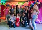 A group of drag performers and their supporters pose for a picture in front of a colorful backdrop