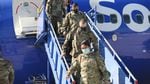 People wearing military camouflage exit an airplane while wearing face coverings.