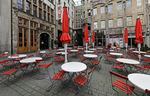 Dozens of tables and chairs are empty in a city square surrounded by old-fashioned European-style stone buildings.