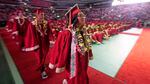 A line of high school students wearing red gowns walks to receive their diplomas.