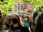 A group of people outdoors and wearing face masks appear to be angry, and one holds a protest sign reading, "My body, my choice, my freedom, my voice, mind your own uterus."
