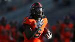 The Oregon State running back wearing a black and orange number five jersey runs with the ball in his left hand.