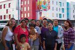 In this photo provided by Michelle Angela Ortiz, Ortiz, left, stands next to the Cully residents she depicted in her mural, "Together We Bloom," at Last Adelitas in Northeast Portland.