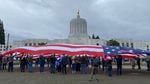 Protesters in Salem on Jan. 1, 2021, stand together underneath a giant U.S. flag in front of the Oregon Capitol building.