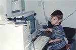 A child sits at a large 1980s desktop computer.