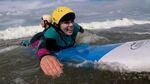 A woman prone on top of a surfboard paddles to catch a wave.