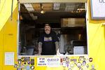The chef and owner of a yellow food cart stands inside, looking to camera.