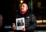 A man who lost his mother to COVID-19 in 2021 holds a photo of her an outdoor night-time event held on the second anniversary of the first COVID-19 case in Portland.