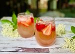 A glass with strawberries, ice, liquid and elderflowers
