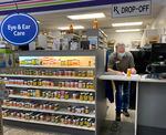 A pharmacist fills out paperwork behind a counter that's next to a shelf full of vitamins and medicines.