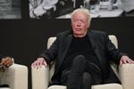 Wearing all black, Phil Knight sits on a chare on stage.