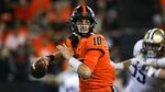 The Oregon State football quarterback wearing an orange and black number 10 jersey holds the ball in his right hand.