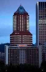 An exterior image of a Marriott Hotel with a skyscraper rising behind it.