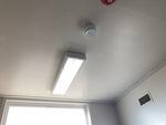 A large white sensor is attached to a bathroom ceiling near a fluorescent light.