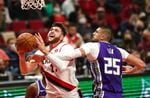 A bearded basketball player in a white Trail Blazers uniform moves the ball towards the hoop as a player in a purple Sacramento Kings uniform tries to block him.