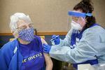 A health-care worker in full protective clothing administers a vaccine to a seated person wearing a mask.