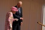 Joe Biden walks to the left of Queen Elizabeth II, offering his arm to her.