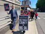 Multnomah County Chair Jessica Vega Pederson, right, and District Attorney Mike Schmidt hold signs announcing the county's lawsuit against fossil fuel companies in Portland, Ore., Thursday, June 22, 2023. The county is suing 17 oil and gas companies, alleging the burning of their products contributed to a deadly heat wave in 2021.